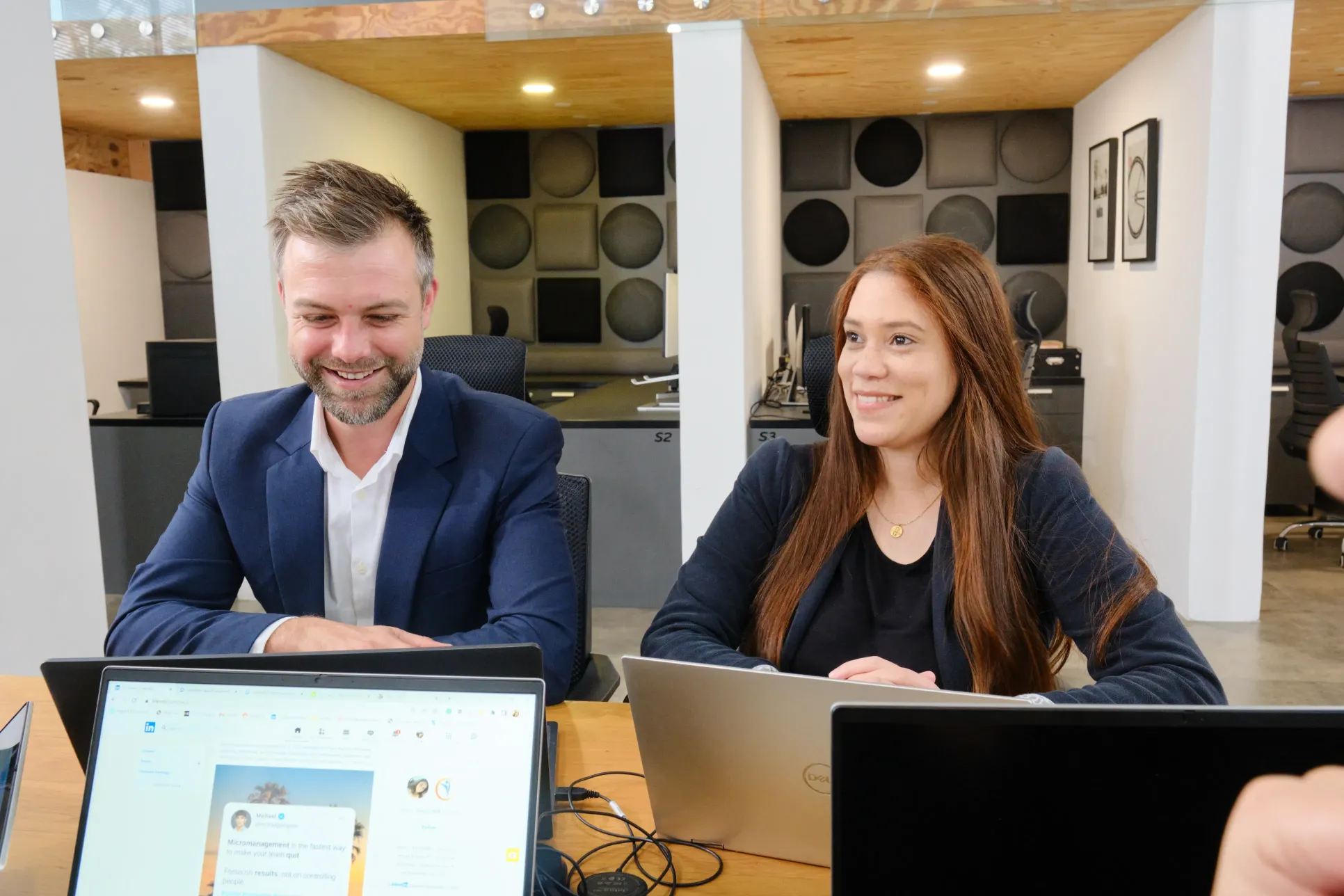 Two people sitting at a desk with laptops in front of them.	